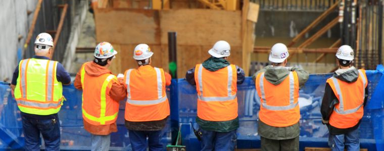 A group of construction workers in hard hats and safety vests looking at a job site A group of construction workers in hard hats and safety vests looking at a job site